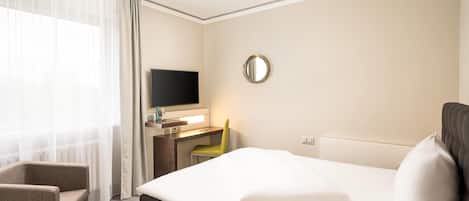 A hotel room with a bed, a desk, a chair, a television, and a mirror.