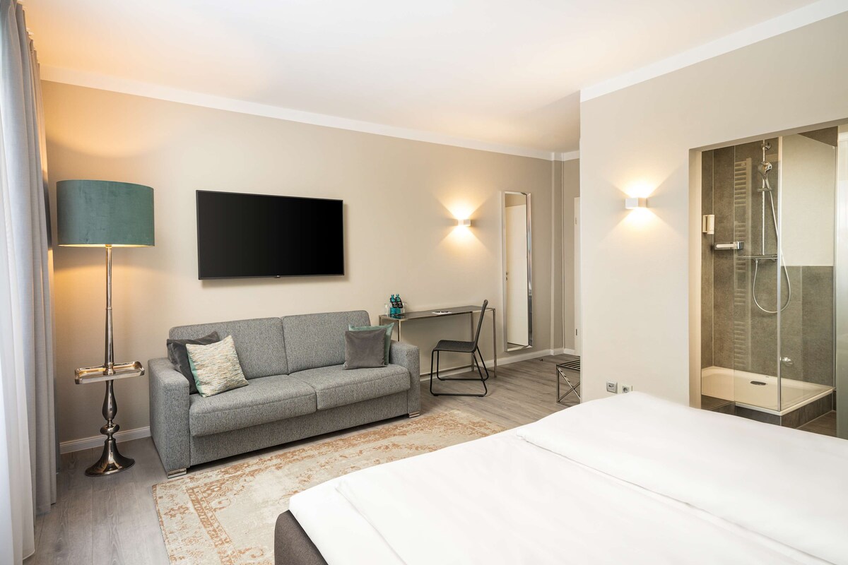 Ein Hotelzimmer mit Bett, einer Couch, einem Schreibtisch, einem Fernseher und einem Duschbereich.