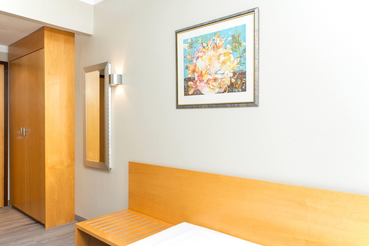 Une chambre d’hôtel avec un lit, une tête de lit en bois, une lampe fixée au mur et un tableau encadré.