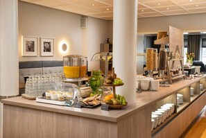 Een buffetgedeelte met een ruim aanbod aan eten en drinken, waaronder een sapdispenser, schalen met fruit en diverse drankjes.