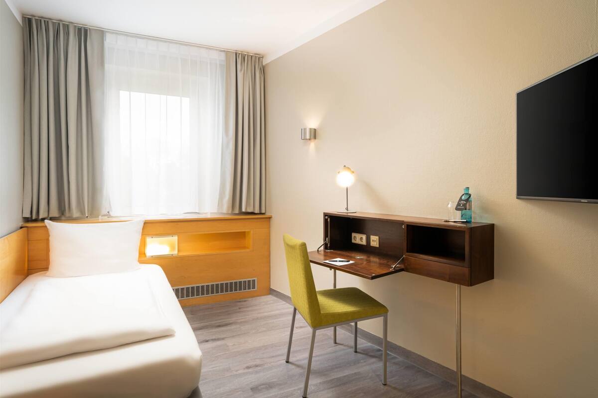 Habitación de hotel con cama, escritorio, silla, televisor y ventana con cortinas.
