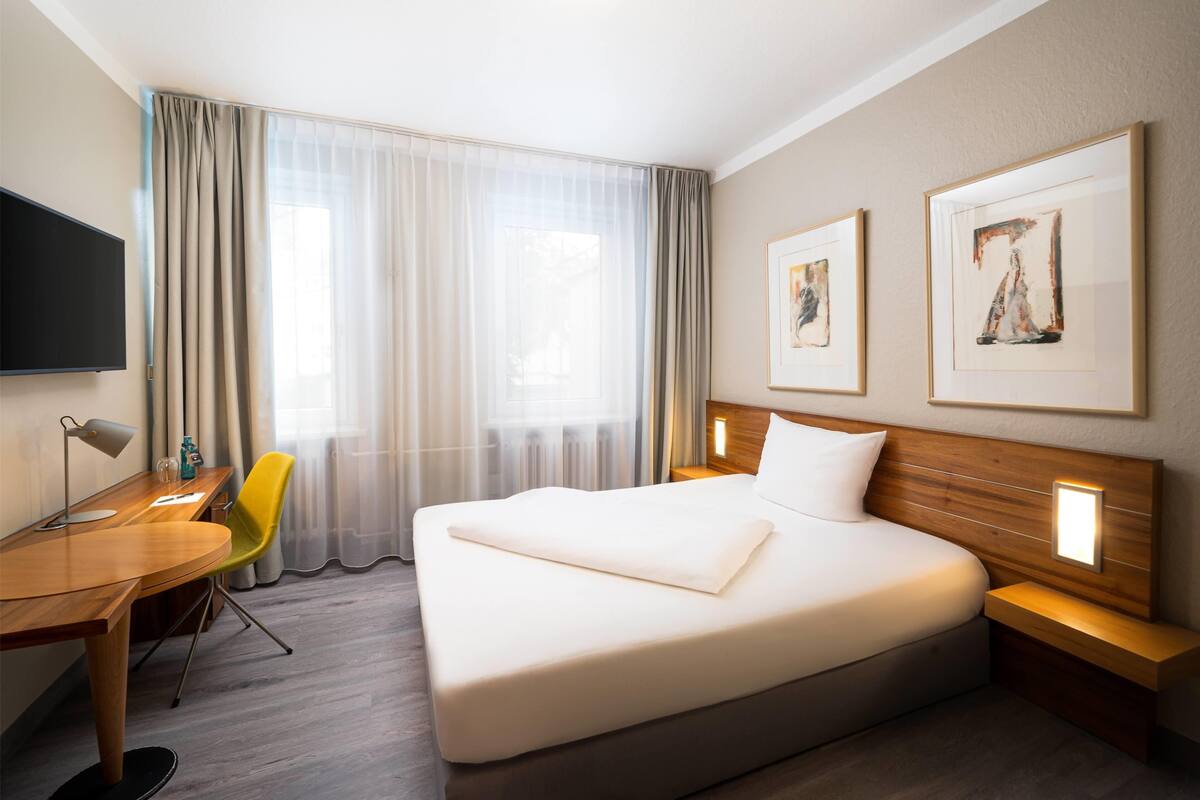 Habitación de hotel con una cama grande, un escritorio con silla, un televisor y dos obras de arte enmarcadas en la pared.