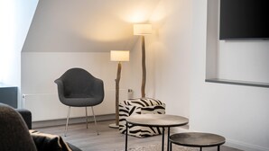 Un intérieur moderne avec un plafond en pente, un fauteuil noir, un pouf à motifs zébrés, une petite table ronde et un lampadaire.