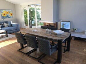 Een moderne woonkamer met een houten eettafel, grijs gestoffeerde stoelen, een blauwe bank en een schilderij van gele bloemen aan de muur.