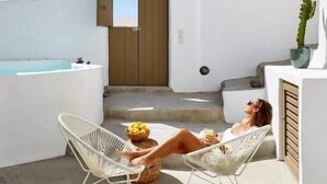 Una terraza en la azotea con una piscina infinita blanca, dos sillones de mimbre blanco y una puerta que da al interior.