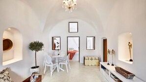 Un salón espacioso con mesa de comedor, sillas blancas, sofá y una mesita de centro. Hay una planta en maceta, un candelabro y obras de arte en las paredes.