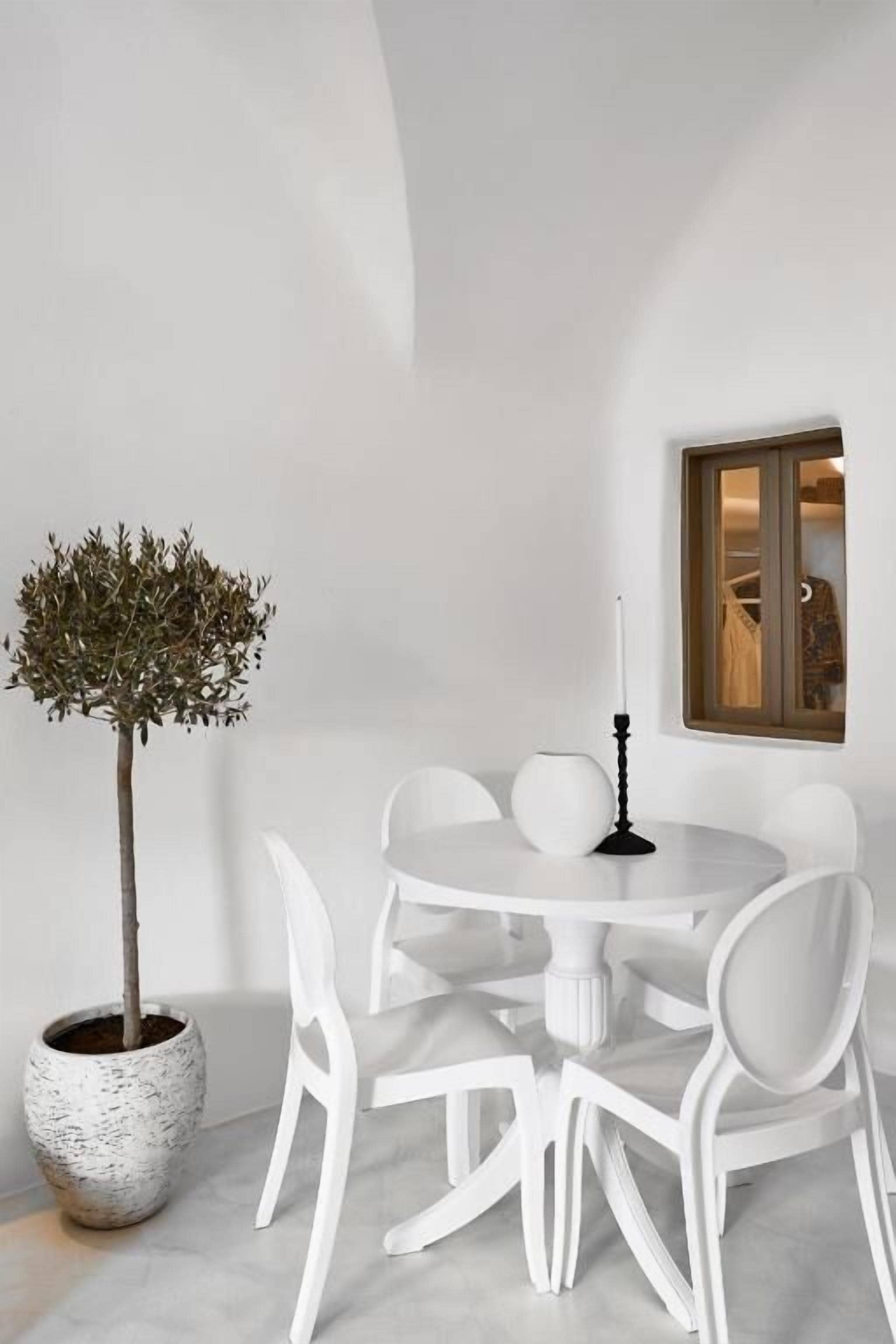 A round white table with six chairs, a potted tree, and a candle on the table.