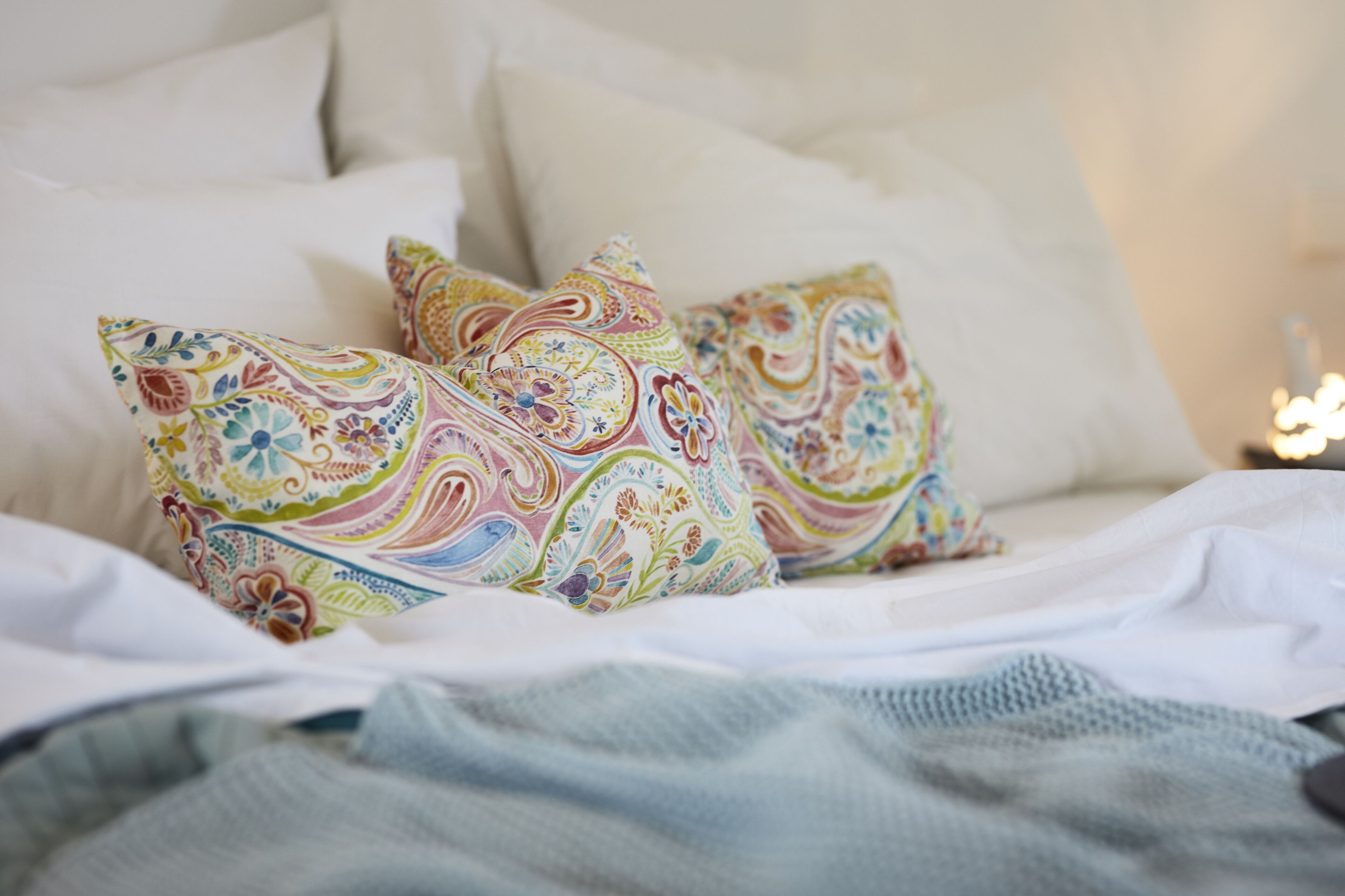 Una cama con ropa blanca y almohadas de colores con diseños.