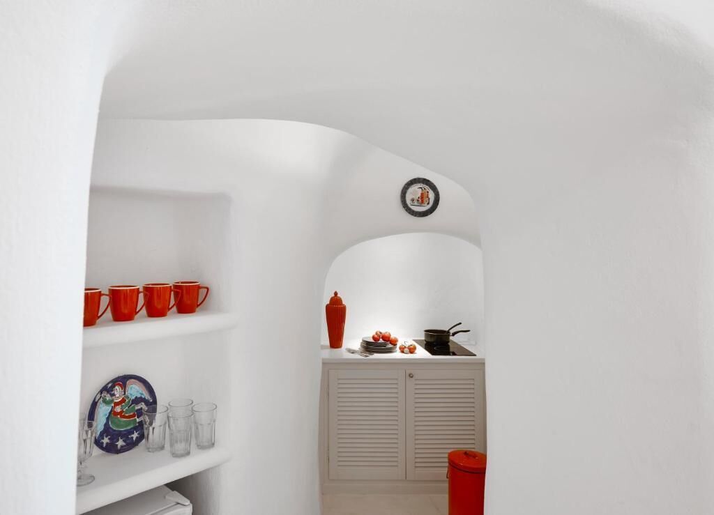 A compact kitchen with white cabinetry, a small countertop, and a red kettle.
