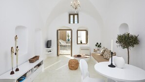 Amplia sala de estar con techo abovedado, una araña, un conjunto de sofás, un televisor y una mesa de comedor.