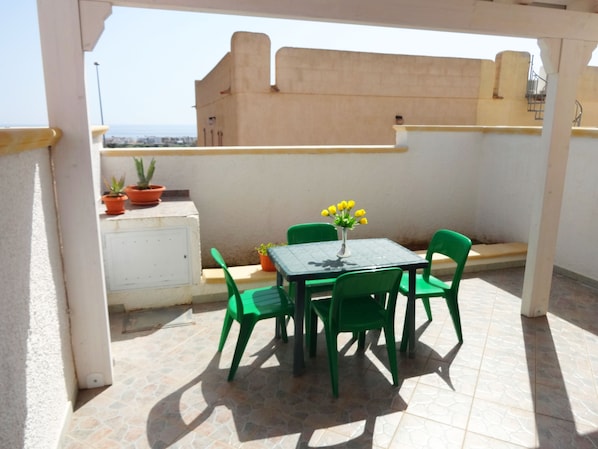A small outdoor patio with a table and chairs, potted plants, and a view of the cityscape.