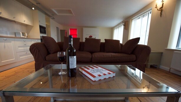 A modern living room with a glass coffee table, a bottle of wine, and a book. - No1 Dove Street (Ipswich)