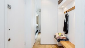 A hallway with a wooden floor, a bench, a wall-mounted bag, and a shelf with items. - Modern Holland Park apartment (London)