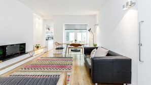 A modern living room with a sofa, TV, and a dining area with a table and chairs. - Modern Holland Park apartment (London)