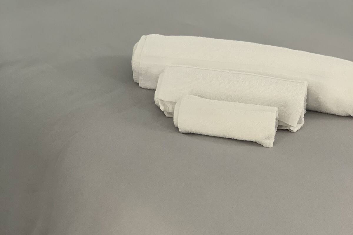 A neatly made bed with grey sheets and white towels, accompanied by floral patterned pillows.