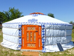 Une yourte traditionnelle, reconnaissable à sa porte orange distinctive et à ses motifs décoratifs, installée dans une zone herbeuse.