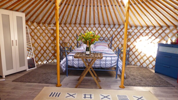 A cozy room with a bed, a table with a vase of flowers, and a wardrobe. - Les Yourtes d'Agnac (Agnac)