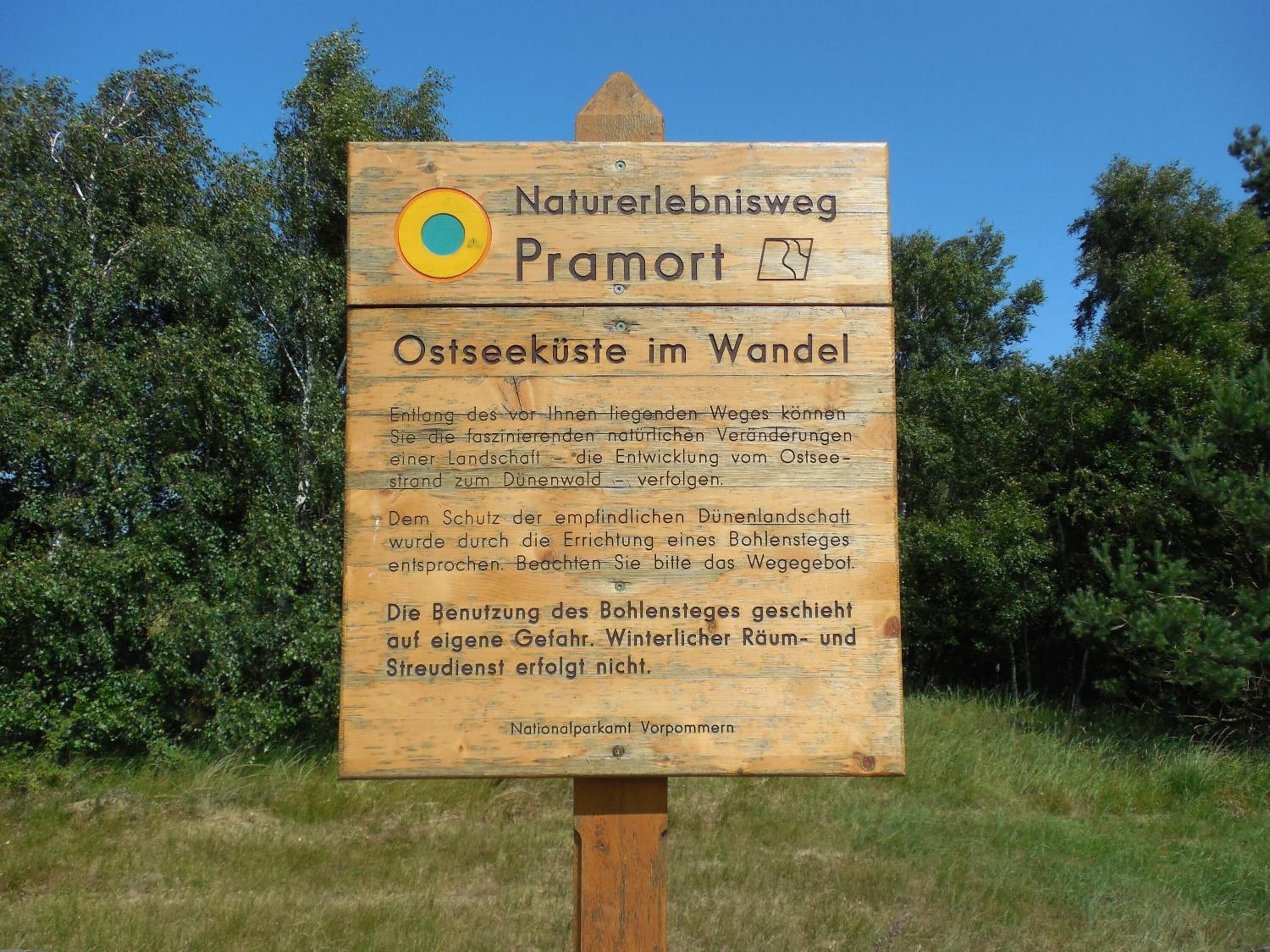 Et træskilt med tekst på tysk, sandsynligvis med information om en natursti eller park.