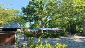 Une cour dallée de pierres, des espaces de détente en plein air sous des parasols et un grand arbre qui offre de l’ombre.