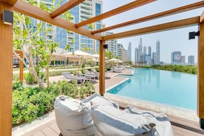 A poolside area with lounge chairs and umbrellas, overlooking a city skyline.
