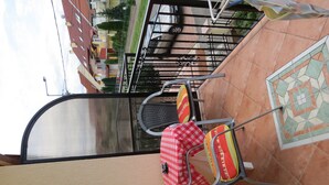 Ein Balkon mit Fliesenboden, Metallstühlen und einer rot-weißen Karotischdecke.