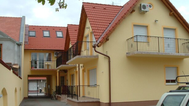 Ein gelbes Gebäude mit roten Ziegel-Dächern, einem verschlossenen Eingang und einem geparkten Wagen.