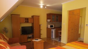 Ein kleines Zimmer mit einem Bett, einer Schlafcouch, einem Fernseher, einer Mikrowelle und einer kleinen Küchenzeile.