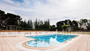 Ein Schwimmbecken mit gefliestem Beckenrand, umgeben von Bäumen und blauem Himmel.