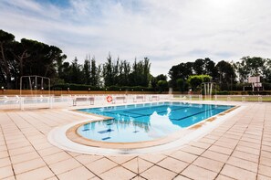 A swimming pool with a tiled deck, surrounded by trees and a clear sky. - Bugalows camping Regio (Santa Marta de Tormes)
