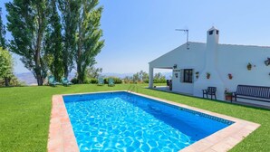 A rectangular swimming pool with a tiled border, surrounded by a well-maintained lawn and a white building with a balcony. - El Encinar Antequera - La Joya by Ruralidays (Málaga)