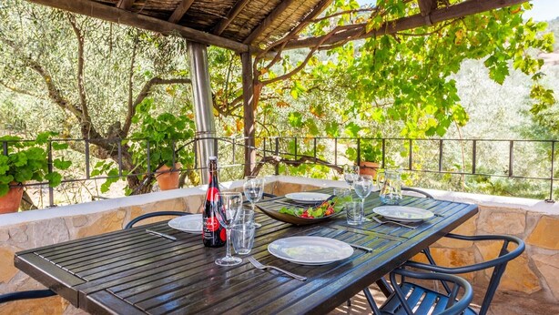 Un espace de restauration en plein air avec une table dressée pour deux personnes, une bouteille de vin et une salade.