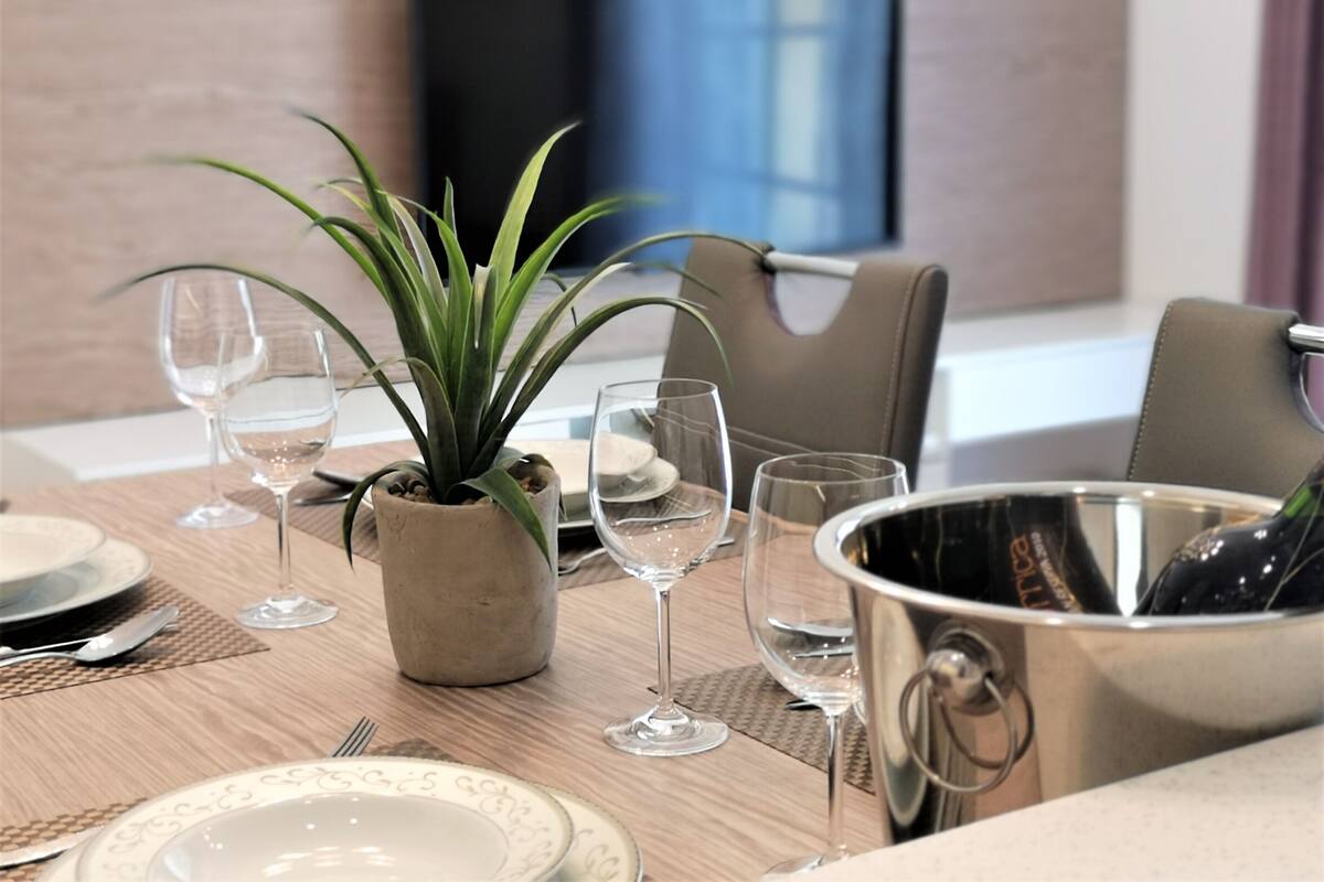 Een eettafel gedekt met borden, wijnglazen, een potplant en een champagnekoeler.