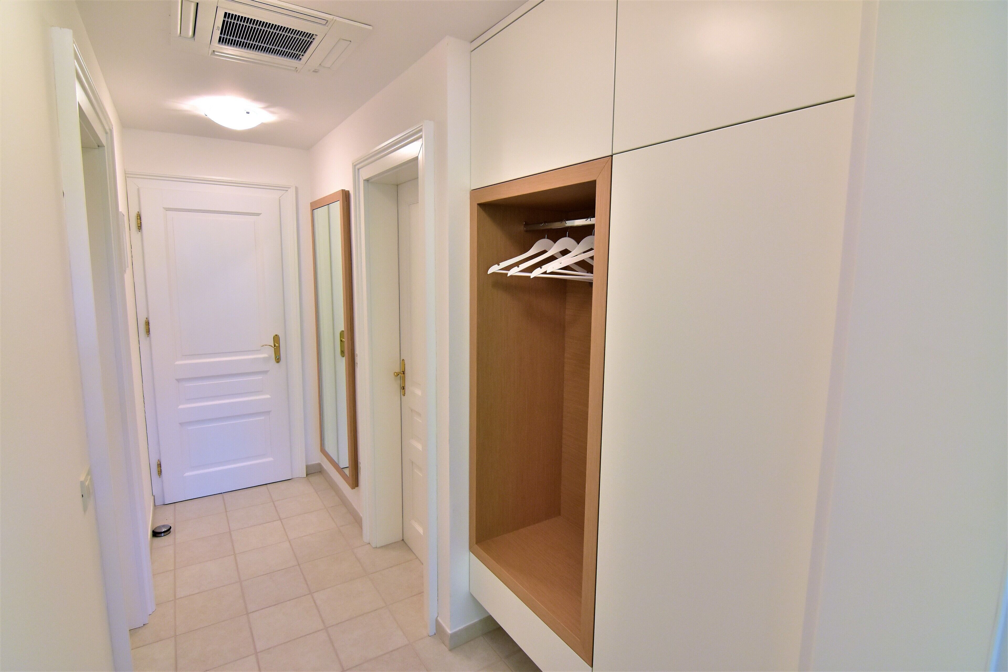 Un couloir avec une porte blanche, une armoire en bois avec une tringle à vêtements et un sol carrelé.