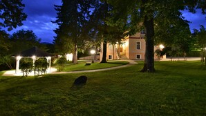 Un espacio exterior bien iluminado con un porche, un árbol grande y un edificio con una escalera.