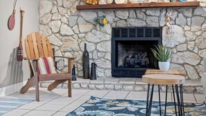 A stone fireplace with decorative items, a wooden chair, a small table, and a patterned rug. - Shady Oaks - Breezy retreat w patio & beach access (Jacksonville Beach)