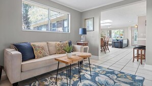 A living room with a sofa, a coffee table, a lamp, and a dining area with chairs and a table. - Shady Oaks - Breezy retreat w patio & beach access (Jacksonville Beach)