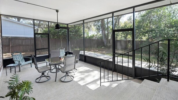 A covered patio with a table and chairs, large windows, and a staircase. - Shady Oaks - Breezy retreat w patio & beach access (Jacksonville Beach)