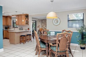 A kitchen with wooden cabinets, a central island, bar stools, and a dining table with wicker chairs.