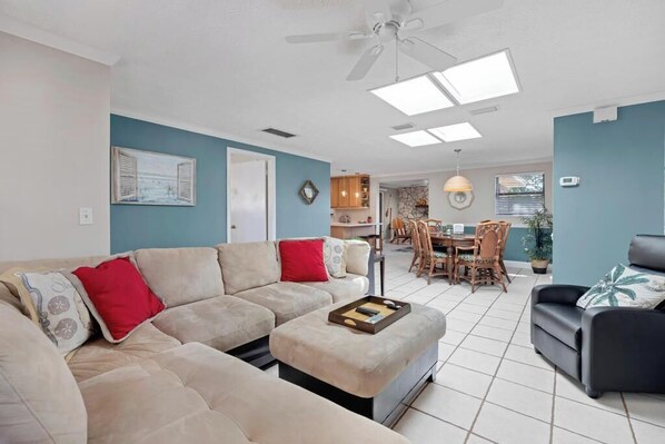 A living room with a beige sofa, a black armchair, a coffee table, and a dining area with wooden chairs and a table.