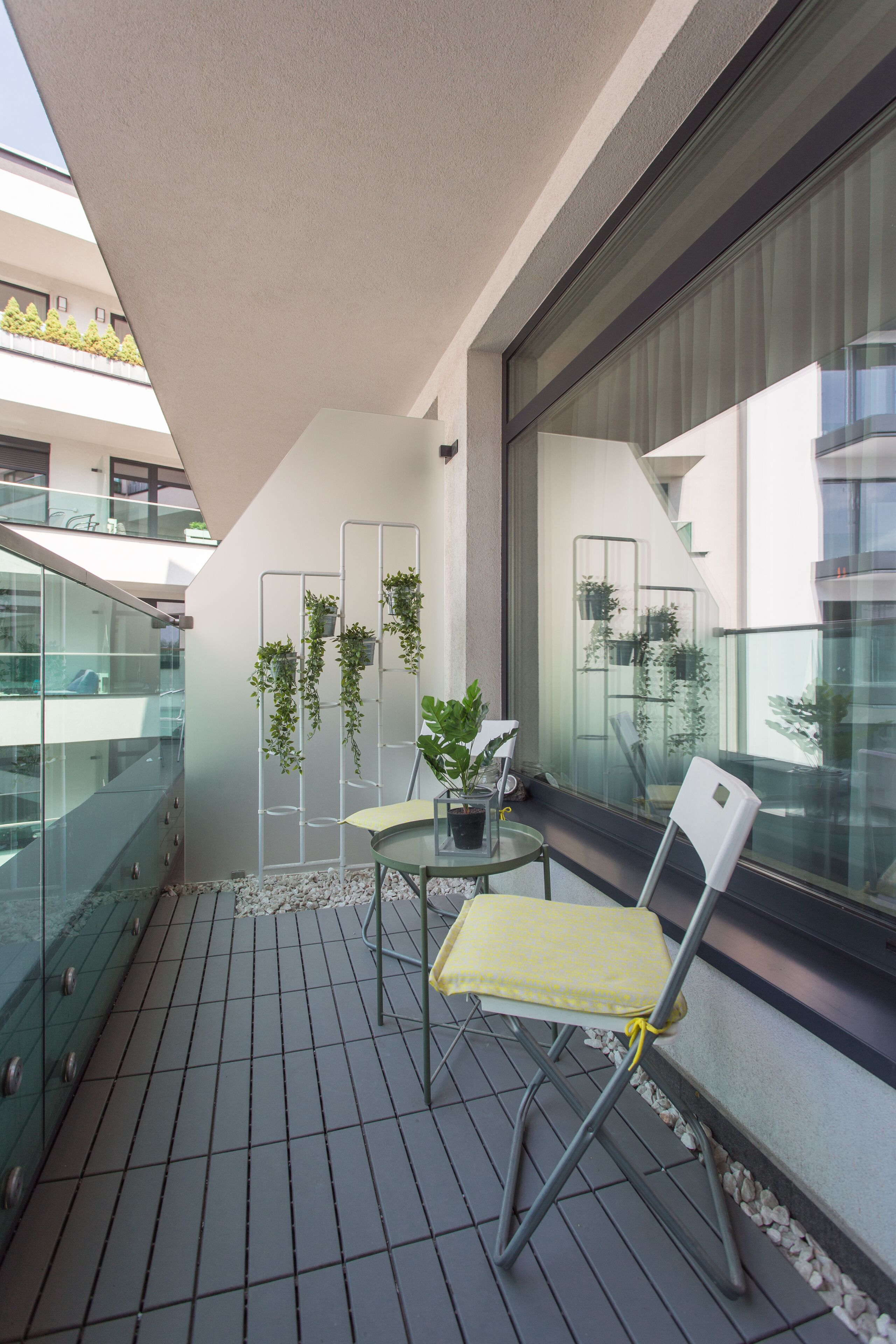 A balcony with a glass railing, a small table with chairs, and potted plants.