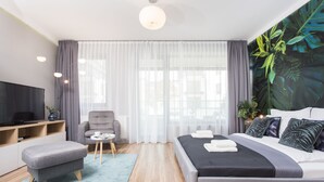 A modern hotel room with a bed, a TV, a seating area, and a large window with curtains. - Studio Apartment, 15 min. walk to Main Square, 10 min. walk to Jewish Quarter (Grzegórzki)