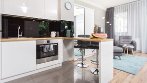 A modern kitchen with white cabinets, a wooden countertop, and a built-in oven. There is a dining area with a table, chairs, and a small side table. - Studio Apartment, 15 min. walk to Main Square, 10 min. walk to Jewish Quarter (Grzegórzki)