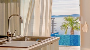 A bathroom with a sink, mirror, and view of a pool and palm tree.