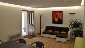 A modern living room with a sofa, a dining table, and chairs. There is a door leading to another room, a floor lamp, and a large abstract painting on the wall. - Chambres D'hôtes Sous L'olivier (Montpellier)