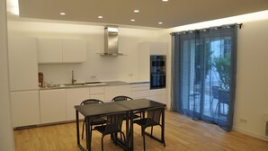 A modern kitchen with white cabinets, a stainless steel range hood, and a dining area with a table and chairs. - Chambres D'hôtes Sous L'olivier (Montpellier)