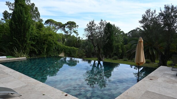 A swimming pool with clear water, surrounded by a tiled deck and lush greenery. - Chambres D'hôtes Sous L'olivier (Montpellier)