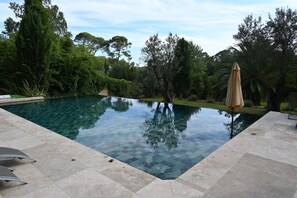 A swimming pool with clear water, surrounded by a tiled deck and lush greenery. - Chambres D'hôtes Sous L'olivier (Montpellier)