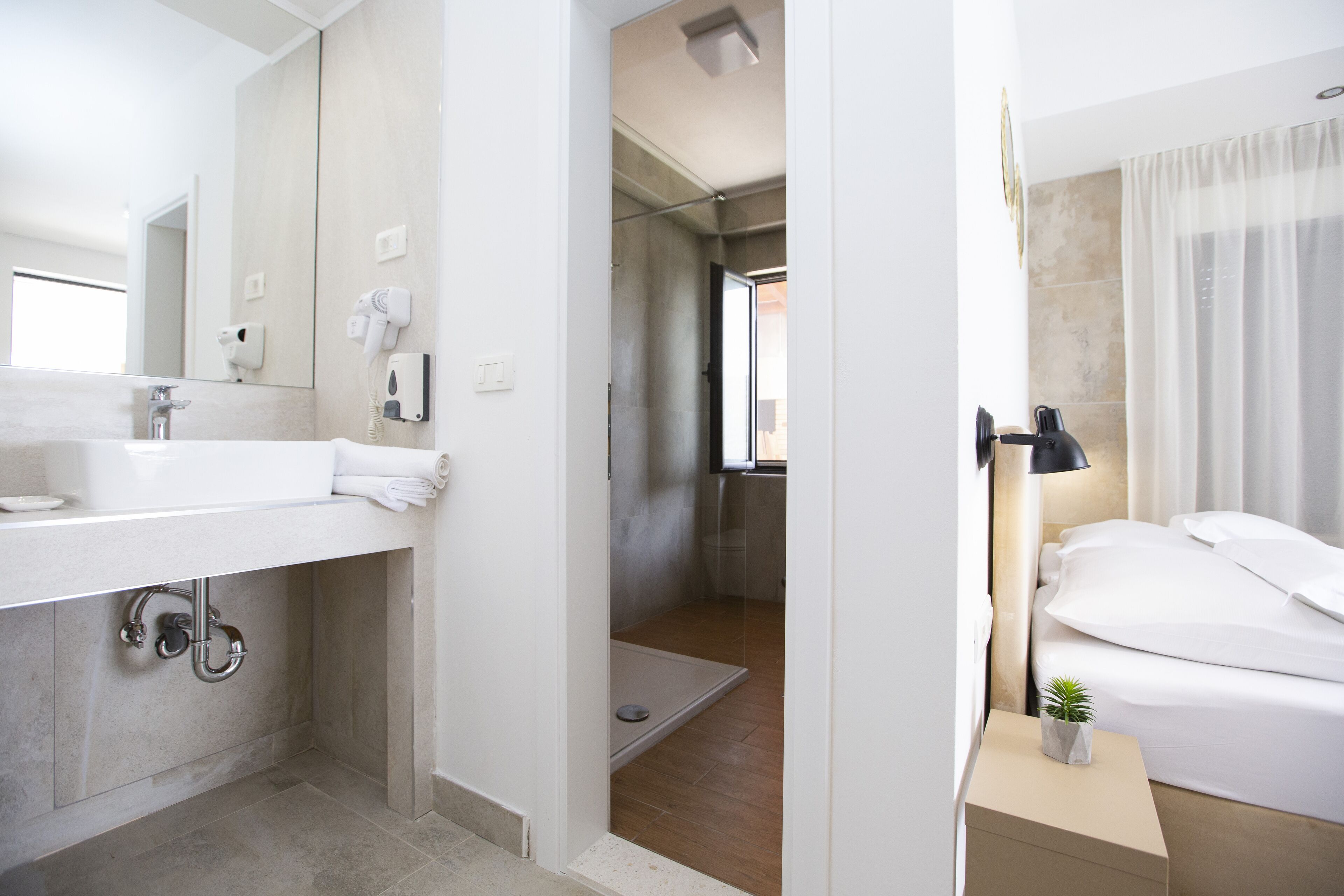 A modern hotel bathroom with a large sink, a hairdryer, and a shower.