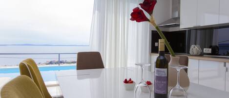 A dining area with a view of the sea, a bottle of wine, and red roses on a white table.