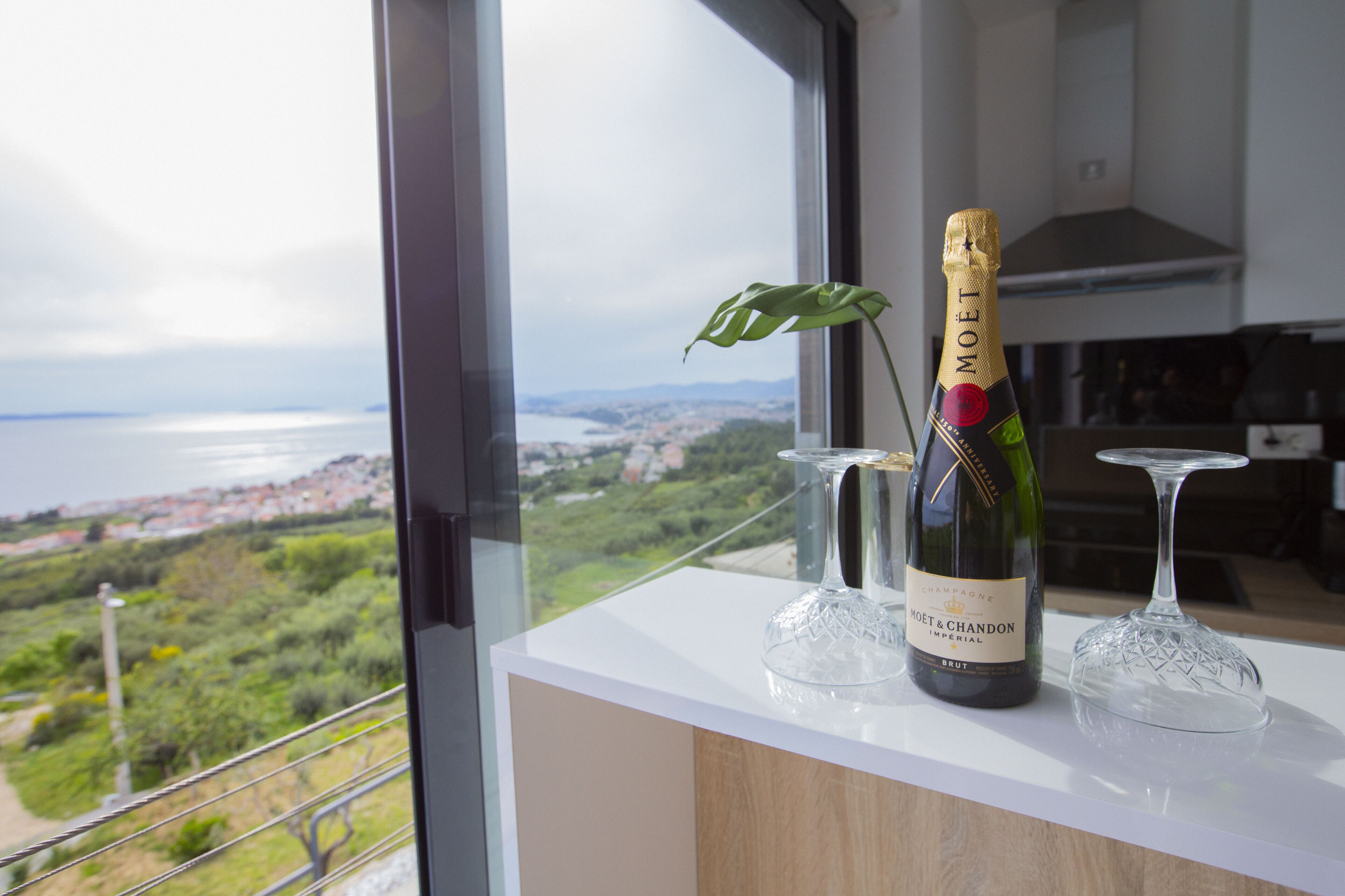 A bottle of Moet & Chandon champagne on a white countertop with a view of a coastal landscape through a window.